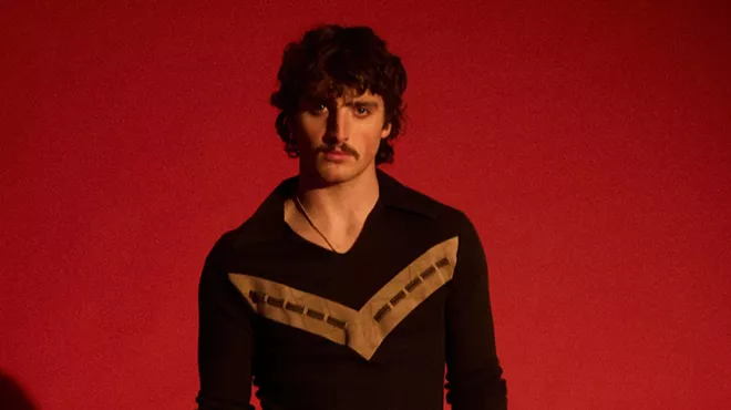 portrait of singer Benson Boone in front of a red background