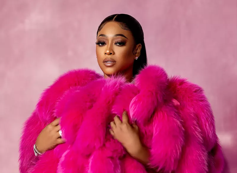 Image: Rapper Trina wearing a pink fur coat while standing against a soft-pink background