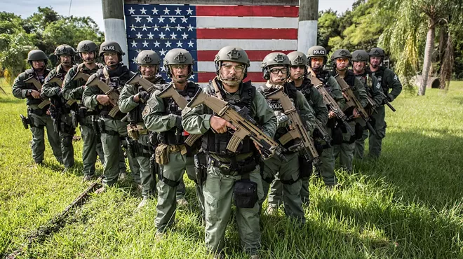 Armed and uniformed U.S. Immigration and Customs Enforcement (ICE) officers standing in the grass in Miami.