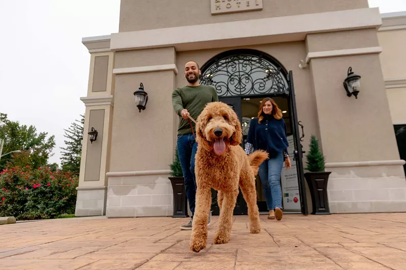 Image: two people walk a dog outside a hotel