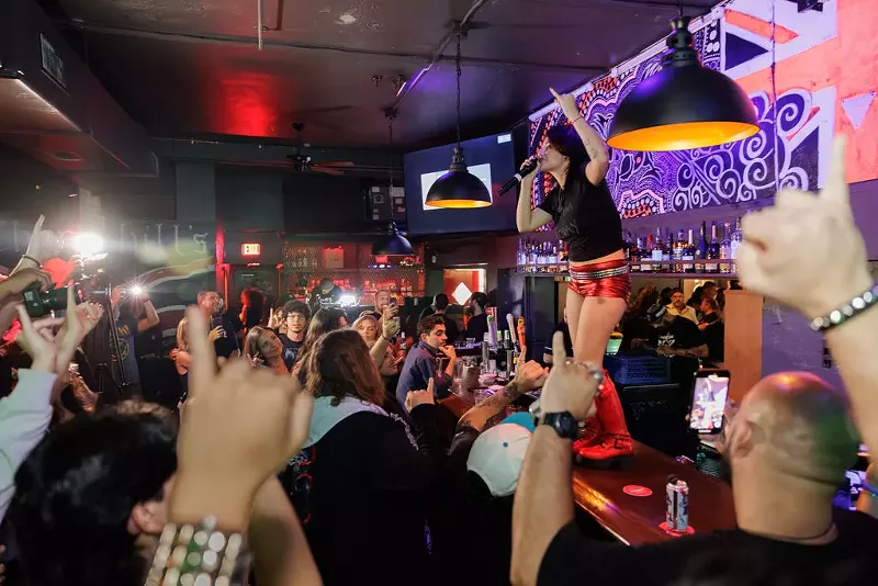 Image: A woman singing on top of a bar surrounded by people.