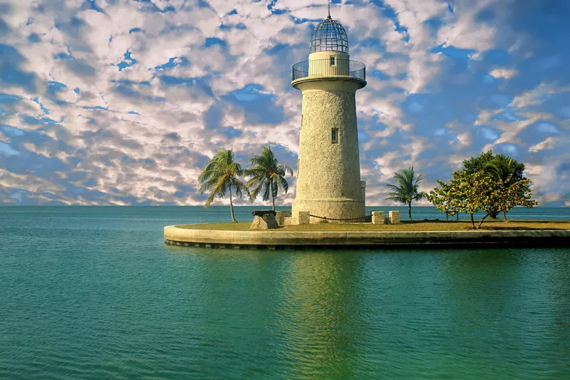 Image: Patches of clouds white clouds on a bright blue sky behind a stout limestone lighthouse