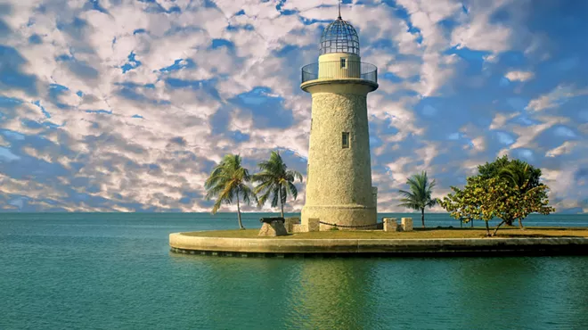 Patches of clouds white clouds on a bright blue sky behind a stout limestone lighthouse