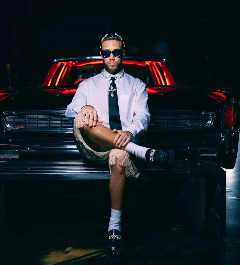 Image: Portrait of Jhayco sitting in front of a car
