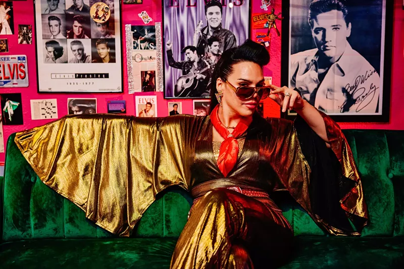 Image: June Rave Romero seated on a couch in a gold jumpsuit and sunglasses