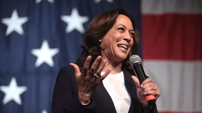 Vice President Kamala Harris speaks into a microphone in front of a U.S. flag