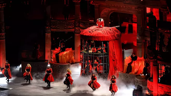 Image of Lady Gaga on stage wearing a red dress that also serves as a cage.