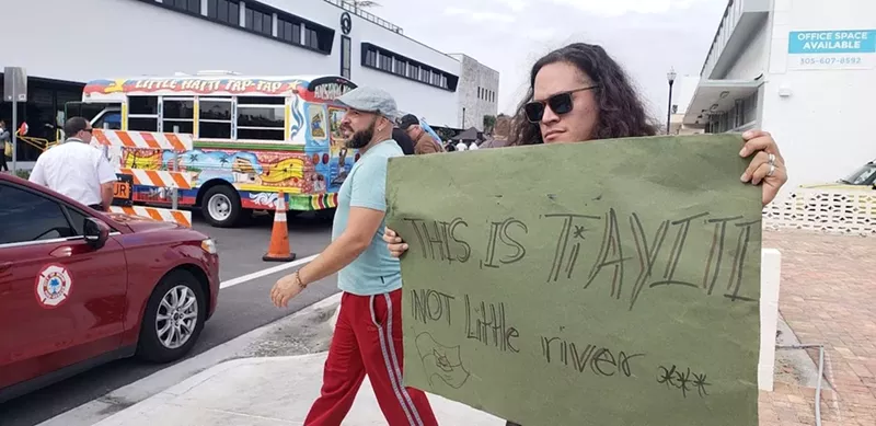 Image: Man holding a signing reading "This is Ti Ayiti"