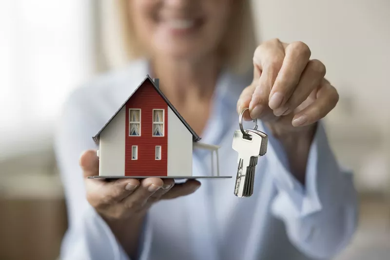 Image: Close up of realtor holding keys and small model of family house in hands, offering apartment for rent, selling, buying.