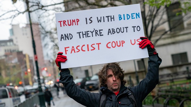 Max Azzarello holds up a sign that reads, "Trump is with Biden, and they're about to fascist coup us."