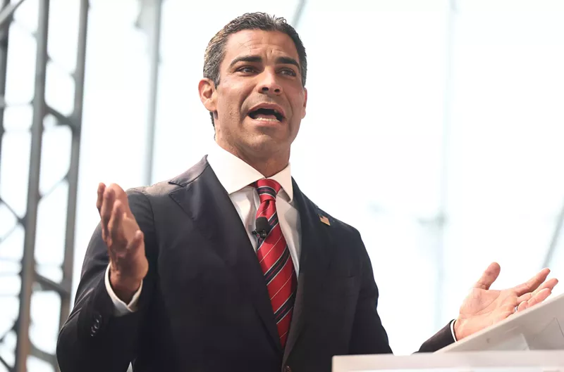 Image: Dressed in a suit and red tie, Miami Mayor Francis Suarez extends his right hand and speaks