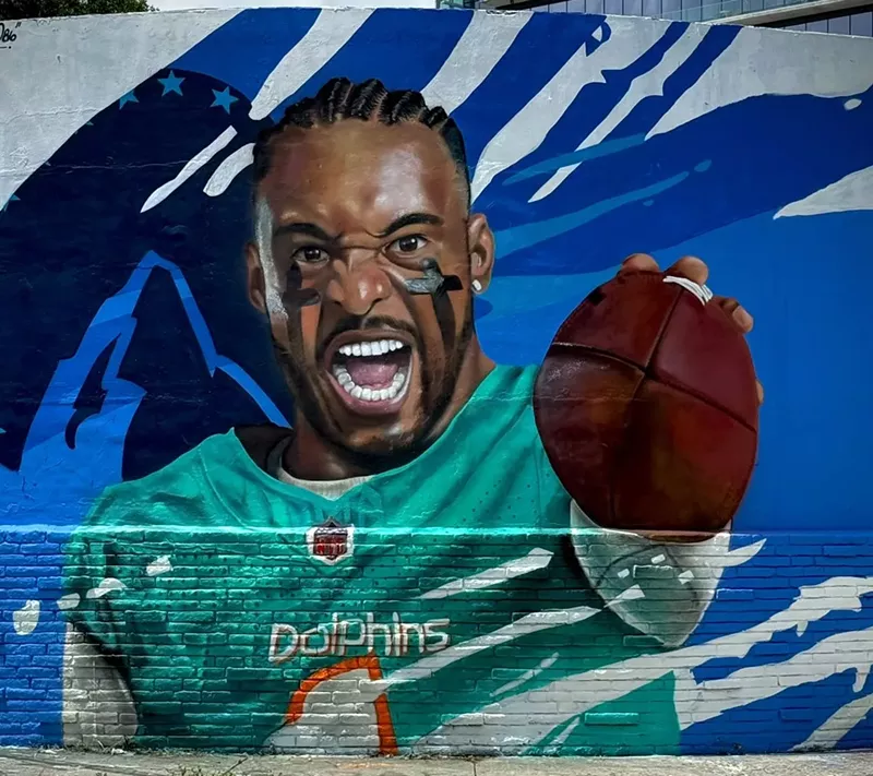 Image: The finished mural of Tua Tagovailoa. He is wearing two black crosses in eyeblack, his mouth is wide open, and he is holding a football.