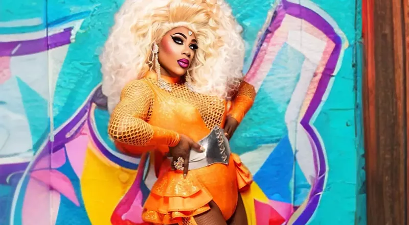 Image: portrait of a drag queen in a blonde wig and orange outfit