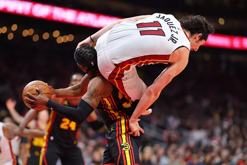 Image: Jaime Jaquez of the Miami Heat is careening in the air during a game, with his derriere positioned on the neck of an Atlanta Hawks player
