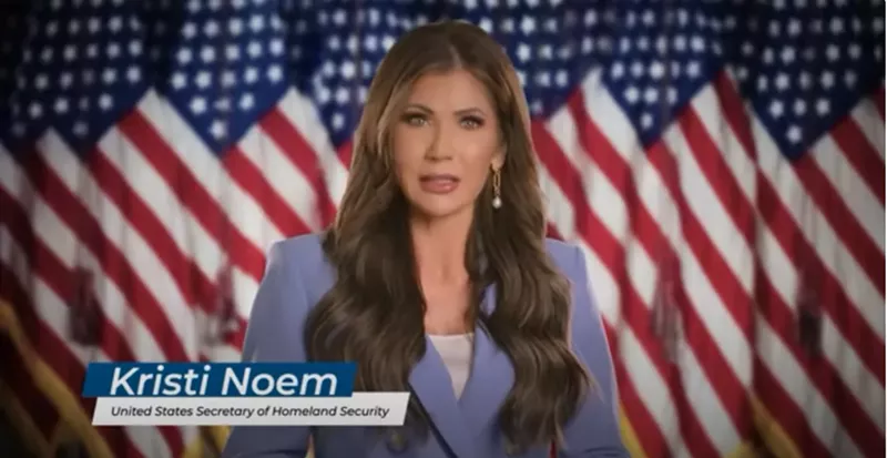 Image: Kristi Noem speaking to the camera with American Flags in the background