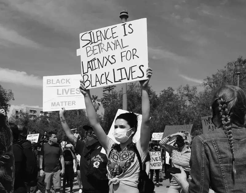 Image: A protester holds up a sign showing Latino solidarity with BLM.