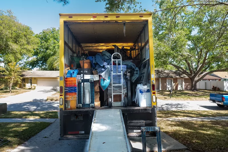 Image: Belongings from a house loaded into a moving van, viewed from the back of the truck, including ramp and dolly.
