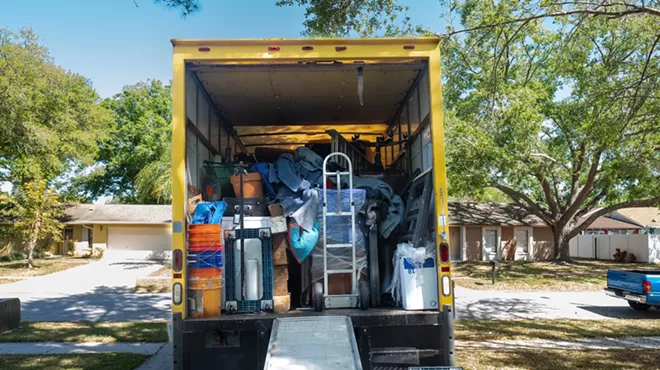 Belongings from a house loaded into a moving van, viewed from the back of the truck, including ramp and dolly.