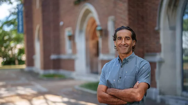 Portrait of a man in a button-down blue shirt standing in front of a brick building
