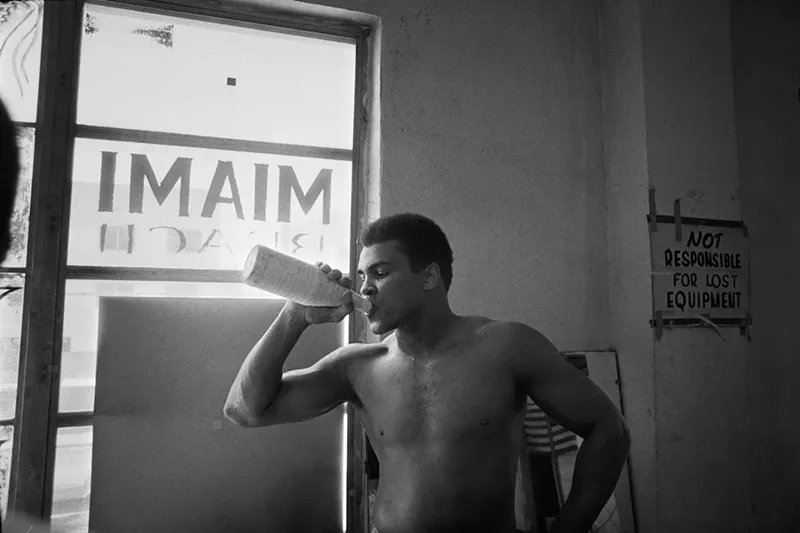 Image: Black and white image of Muhammad Ali in the gym drinking water from a sports bottle