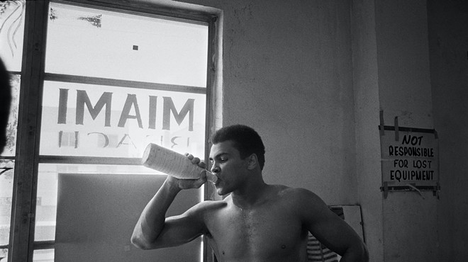 Black and white image of Muhammad Ali in the gym drinking water from a sports bottle