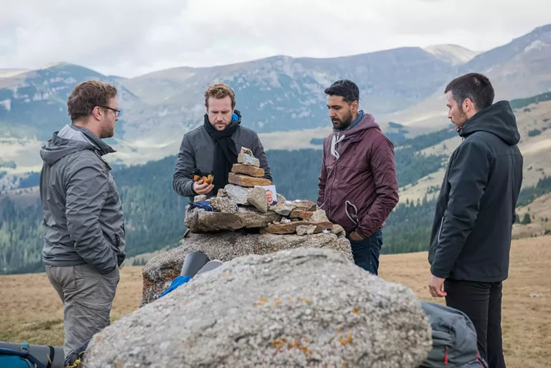 Image: Four British lads — played by Sam Troughton (left), Rafe Spall, Arsher Ali, and Robert James-Collier — hike through the deserted woods of northern Sweden before bashing open the door of a decrepit cabin to spend the night there in The Ritual.