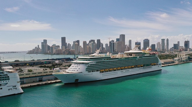 A large cruise ship docked in a port, with the Miami skyline in the background.