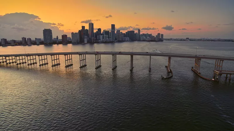 Image: a sunset view of the downtown Miami skyline in 2022 with the Rickenbacker Causeway to Key Biscayne in the foreground