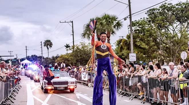 a man on stilts leads a parade route