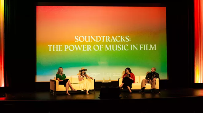 a panel of four people sit on chairs on a stage in front of a projection with the words, "soundtracks: the power of music in film"