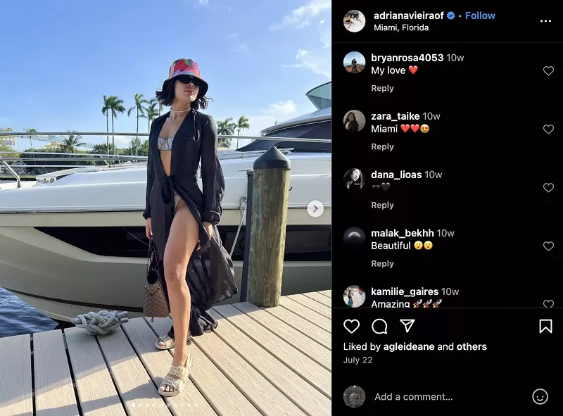Image: instagram screenshot showing a photo of a woman dressed in a bikini covered by a sheer robe, standing on a dock with a boat in the background