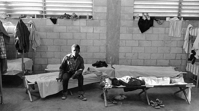 Two men sitting on beds inside what was then known as the INS Krome Detention Camp.