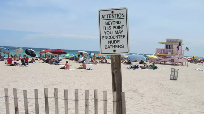 A sign leading to a sandy Miami beach that reads, in all uppercase letters: Attention: Beyond this point you may encounter nude bathers