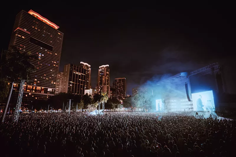 Image: a huge crowd at an outdoor venue with the downtown Miami skyline in the background