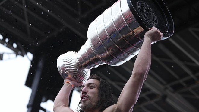 A soggy, shirtless hockey player named Ryan Lomberg hoists the Stanley Cup trophy over his head