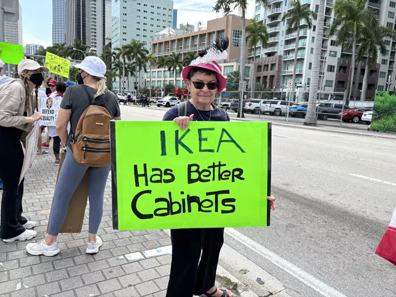 Image: A protester at the Torch of Friendship holds a sign that reads, "IKEA has better cabinets."