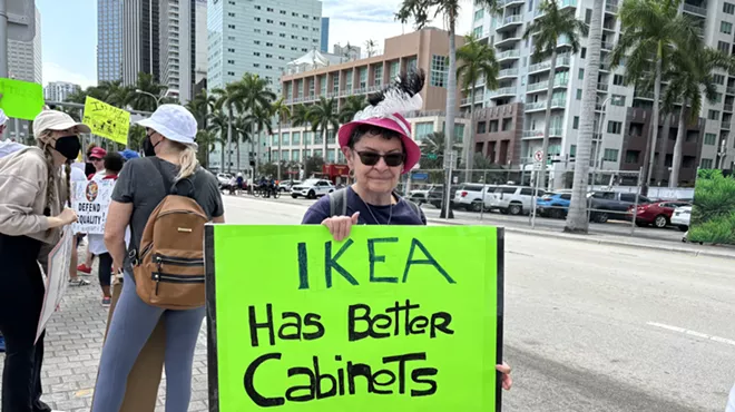 A protester at the Torch of Friendship holds a sign that reads, "IKEA has better cabinets."