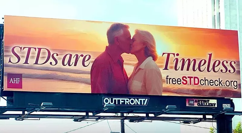 Image: A billboard shows two seniors, a man and a woman, kissing and text that reads "STDs are Timeless"