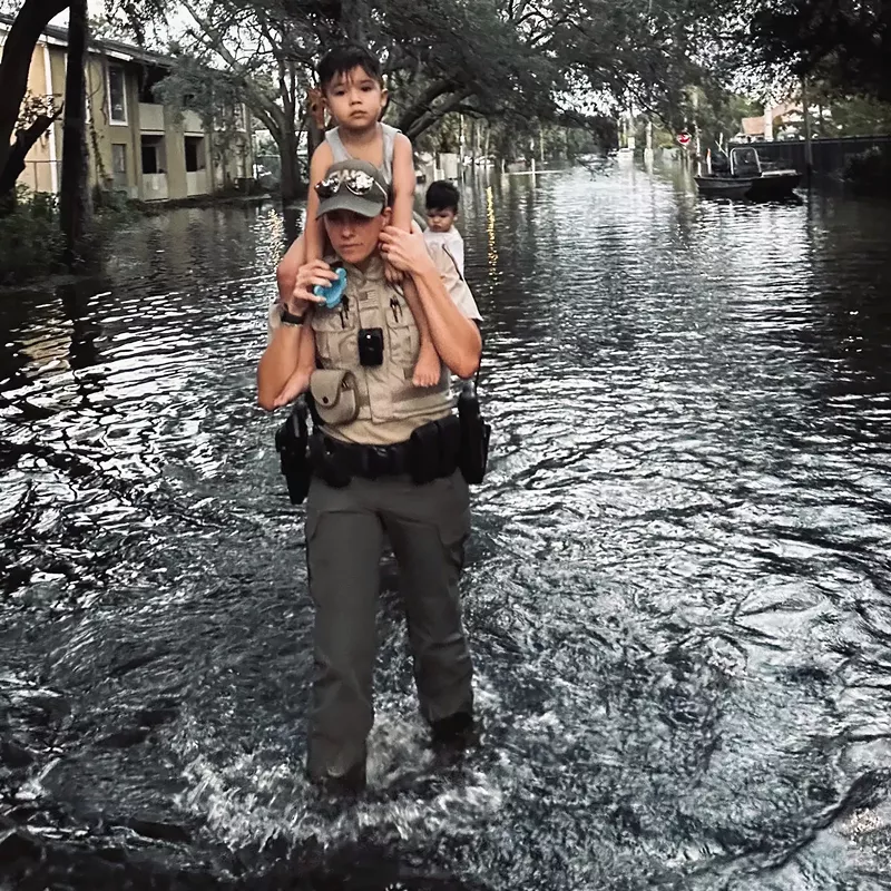 Image: Florida Fish and Wildlife officer carries child on her shoulders through shin-deep water in a flooded street