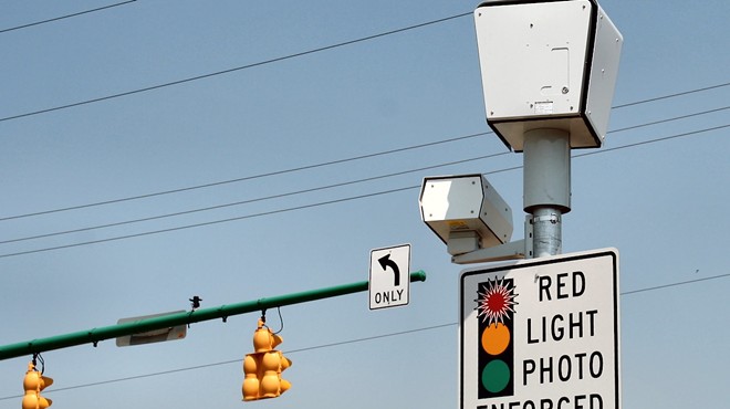 Red light camera with "RED LIGHT PHOTO ENFORCED" sign at intersection