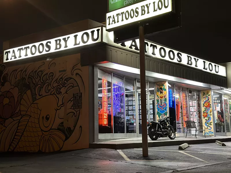 Image: facade of a tattoo shop with three marquees reading "Tattoos By Lou"