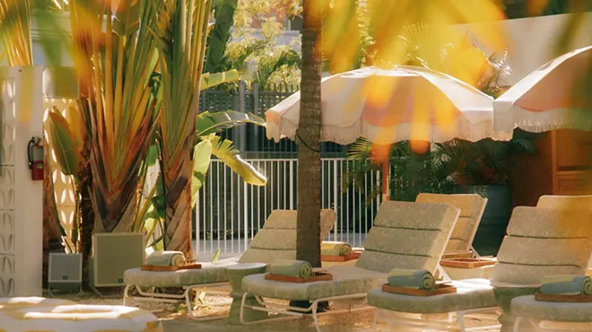 a set of lounge chairs and beach umbrellas surrounded by palms in front of a pool