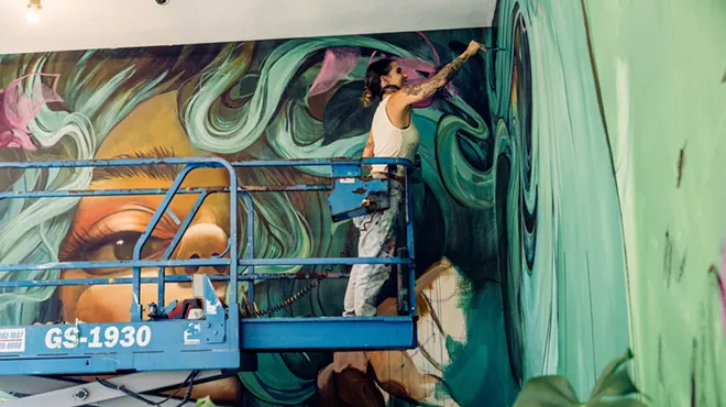 a woman stands on a platform to paint a mural
