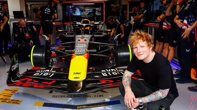 Ed Sheeran crouching down next to a race car