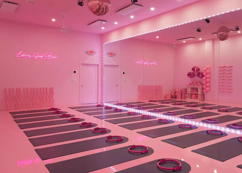 Image: a studio lit in pink lighting with mats on the floor