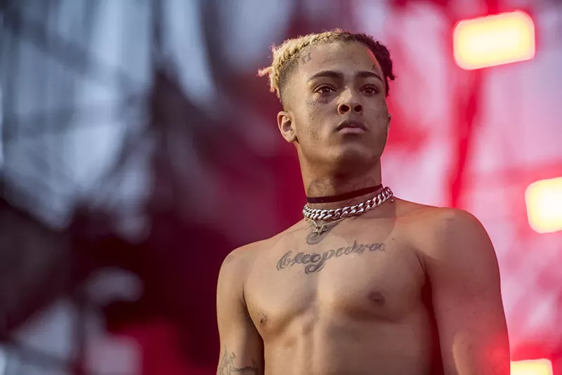 Image: A color photo of popular and controversial local rapper XXXtentacion, head and torso, looking defiant, onstage at the 2017 Rolling Loud hip-hop festival in Miami