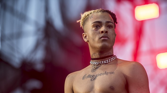 A color photo of popular and controversial local rapper XXXtentacion, head and torso, looking defiant, onstage at the 2017 Rolling Loud hip-hop festival in Miami