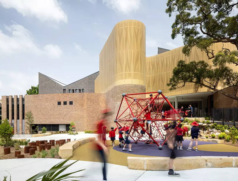 Image: children play on a red jungle gym in front of a building