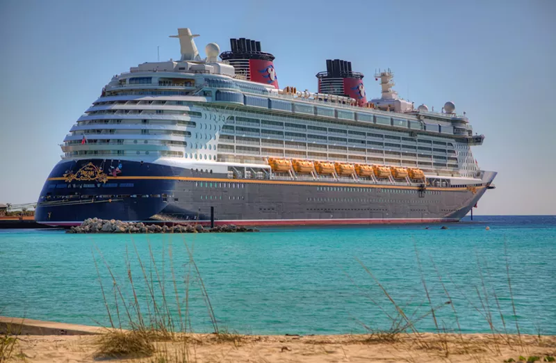 Image: The Disney Dream cruise ship –– a massive vessel colored navy, white, and red –– arrives to shore in turquoise blue waters Castaway Cay, Bahamas.