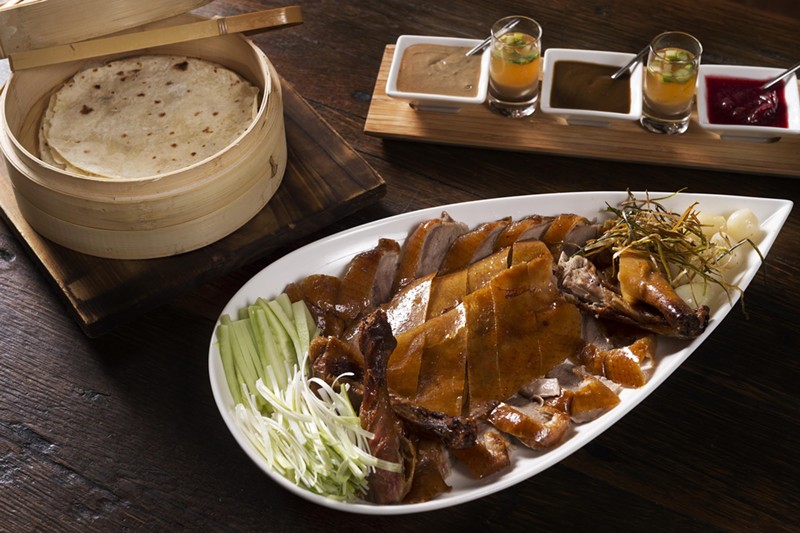 The whole duck, carved to order, is presented on a platter alongside an array of accompaniments — a bamboo basket brimming with hand-rolled pancakes and three distinct sauces: traditional hoisin (plum), cranberry, and peanut-tahini.